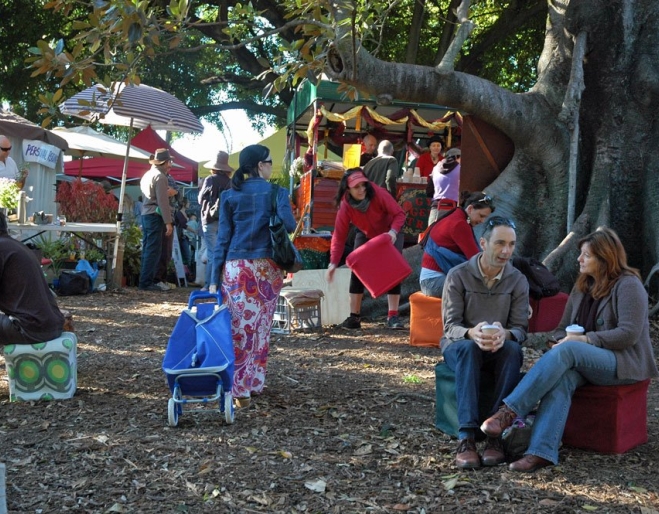 Davies Park Market People sitting under a tree in the Davies Park Market with stalls in the background.