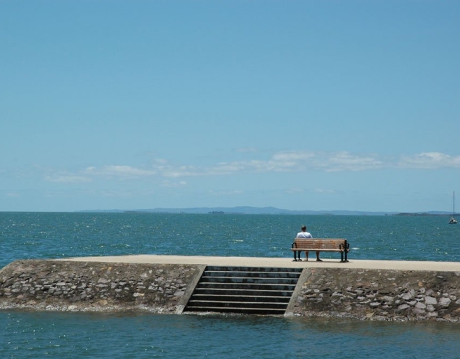 Man sitting on bench looking out to the ocean