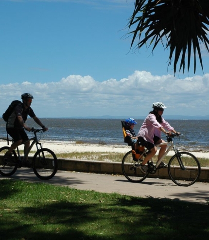 Bribie Island Walk or Cycle Family cycling on cycle path on Bribie Island with Moreton Bay ocean in background.